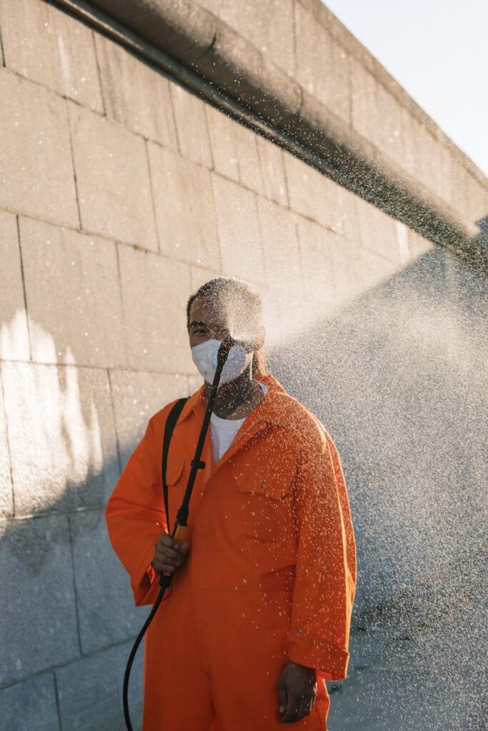Man in a protective mask spraying water against an urban wall, creating mist outdoors.